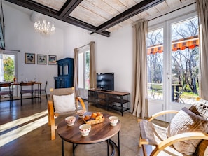 Ein geräumiges Wohnzimmer mit Essbereich, einem Fernseher und einem großen Fenster mit Vorhängen.