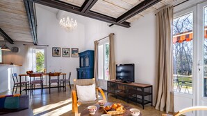 A spacious living room with a dining area, a television, and a large window with curtains. - House in Villars, in the ochre hills of the Luberon, Vaucluse (Villars)