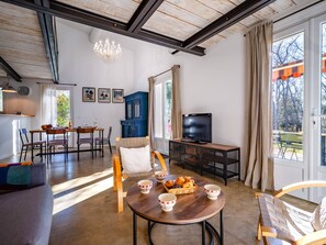 Ein geräumiges Wohnzimmer mit Essbereich, Fernseher und einem großen Fenster mit Vorhängen.