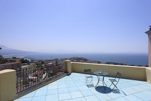A balcony with a table and chairs, a view of the sea, and buildings in the distance. - Spacious apartment in the heart of Petraio, one of Naples' most authentic neighborhoods, just a 10-minute walk from the Vanvitelli metro station and the Petraio funicular. Located in a 19th-century building, it retains vaulted ceilings, fine details and  (Napoli)