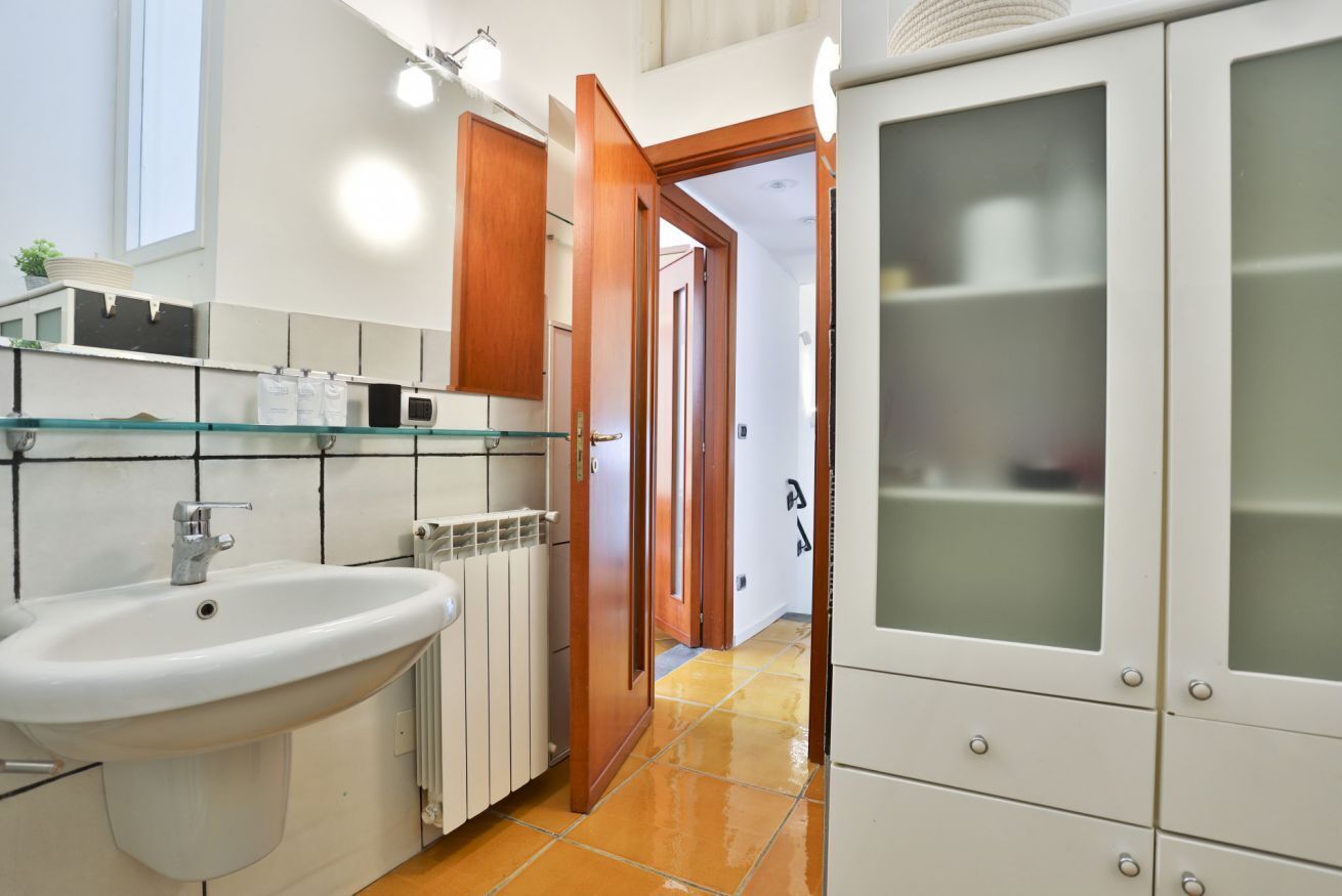 Un bagno con un lavandino bianco, mensole in vetro, una porta in legno e un armadietto con ante in vetro satinato.