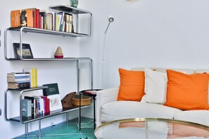 Ein Wohnzimmer mit einem weißen Sofa, orangen Kissen und Metallregalen mit Büchern und Dekoration.