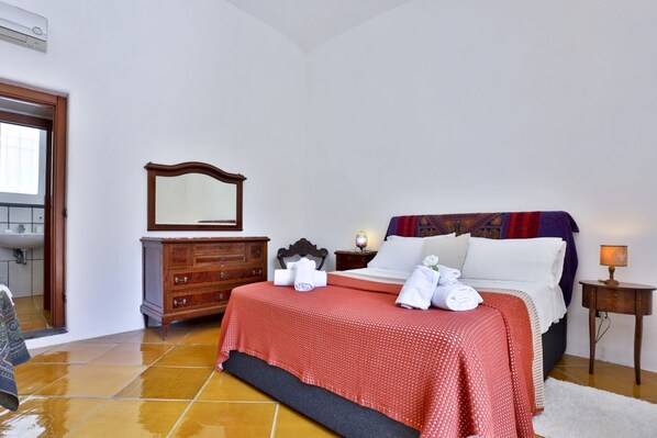 Una habitació d'hotel amb un llit, un taulell de nit, un mirall, una petita còmoda de fusta i una làmpada.