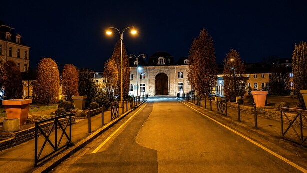 Vista noturna de uma rua que leva a um edifício grande com um arco imponente.