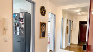 Um corredor com geladeira, porta com espelho e piso de madeira.