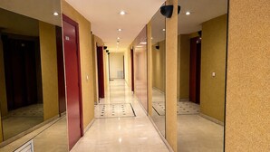 Corredor de hotel com paredes espelhadas, portas vermelhas e chão em mosaico.