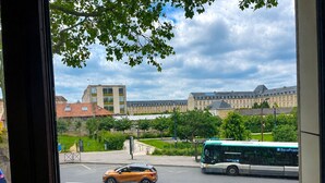 Vista de uma estrada com um carro e um ônibus, edifícios ao fundo e uma árvore em primeiro plano.