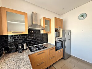 Uma cozinha moderna com armários de madeira, painel de azulejos pretos, eletrodomésticos de aço inoxidável e um relógio na parede.