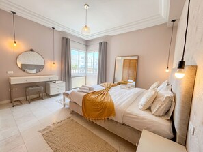 Quarto com cama, mesa de cabeceira, espelho e janela, com vista para o exterior.