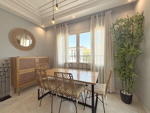 Uma área de refeições com mesa de madeira, cadeiras de vime, um espelho e um vaso com planta.