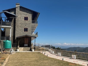 A multi-story stone building with a balcony, a water tank, and a view of mountains.