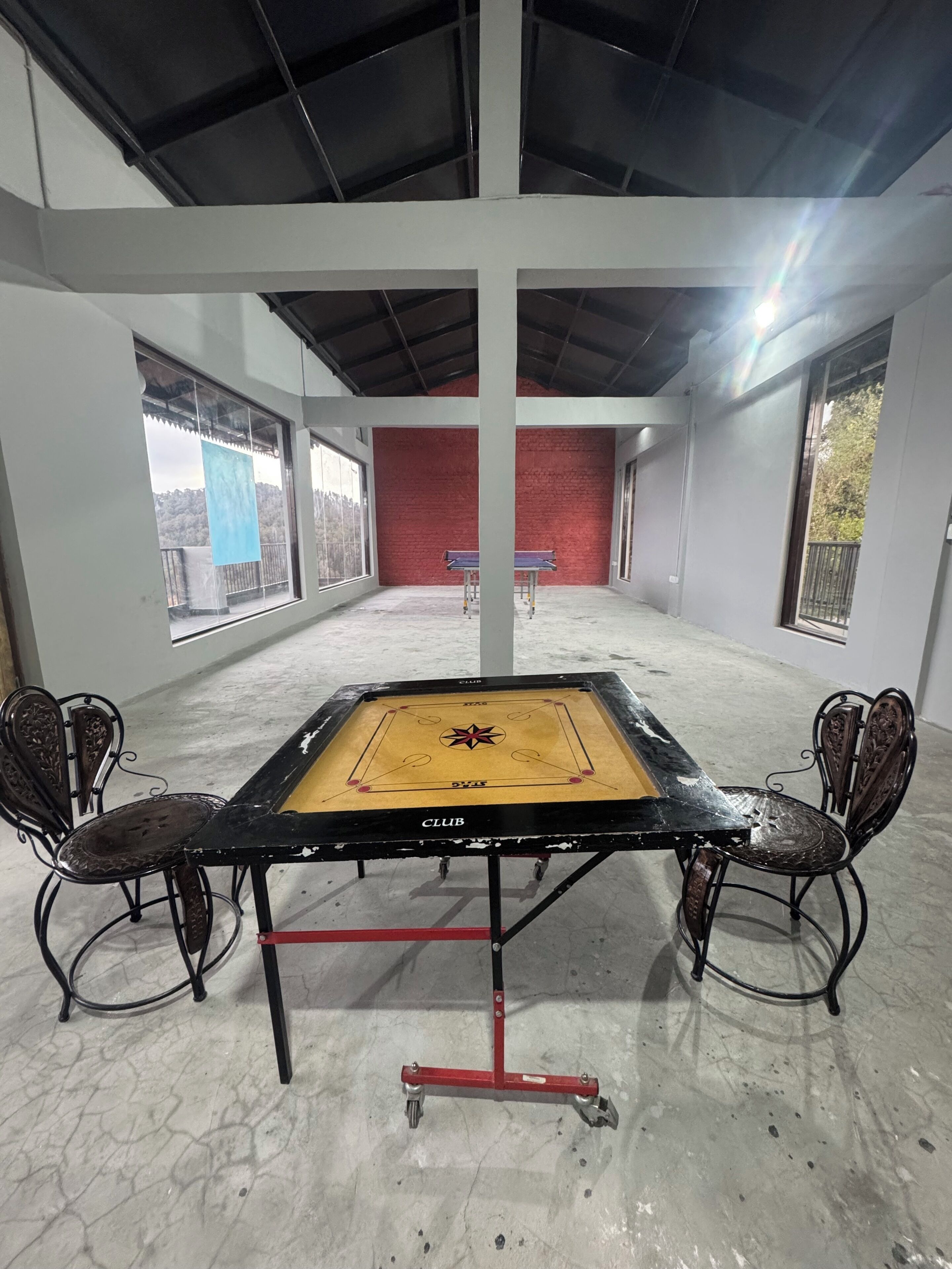 A billiards table with chairs, a red brick wall, and large windows.