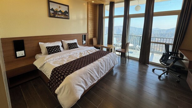 Una camera d'albergo con un letto grande, una scrivania, una sedia e un balcone con vista sulle montagne.