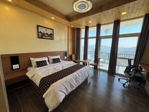 A hotel room with a large bed, a desk, a chair, and a balcony with a view of the mountains. - Ivaan Belle-Vue (Dhari)
