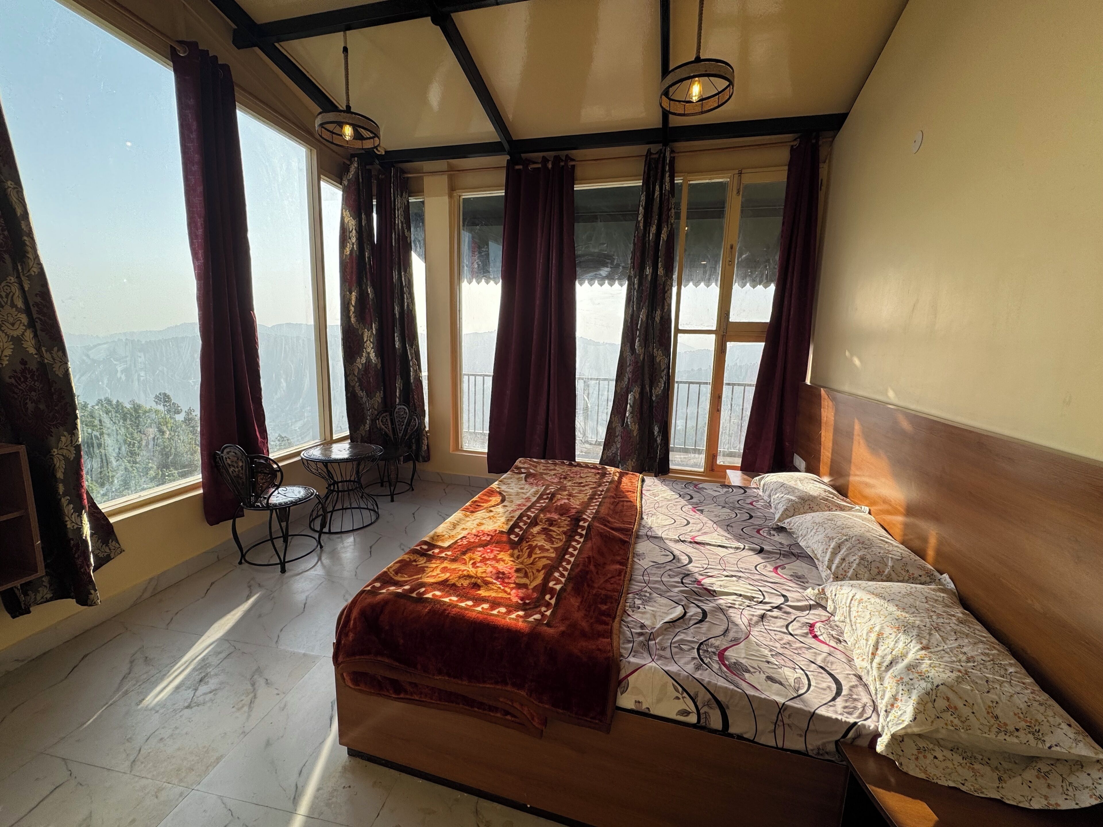 A bedroom with a bed, a small table, two chairs, and a balcony with curtains.