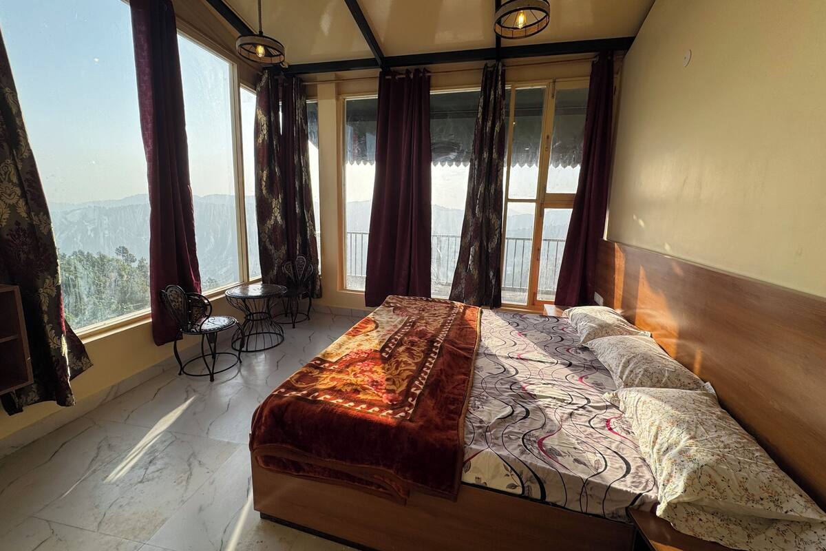 A bedroom with a bed, a small table, two chairs, and a balcony with curtains.