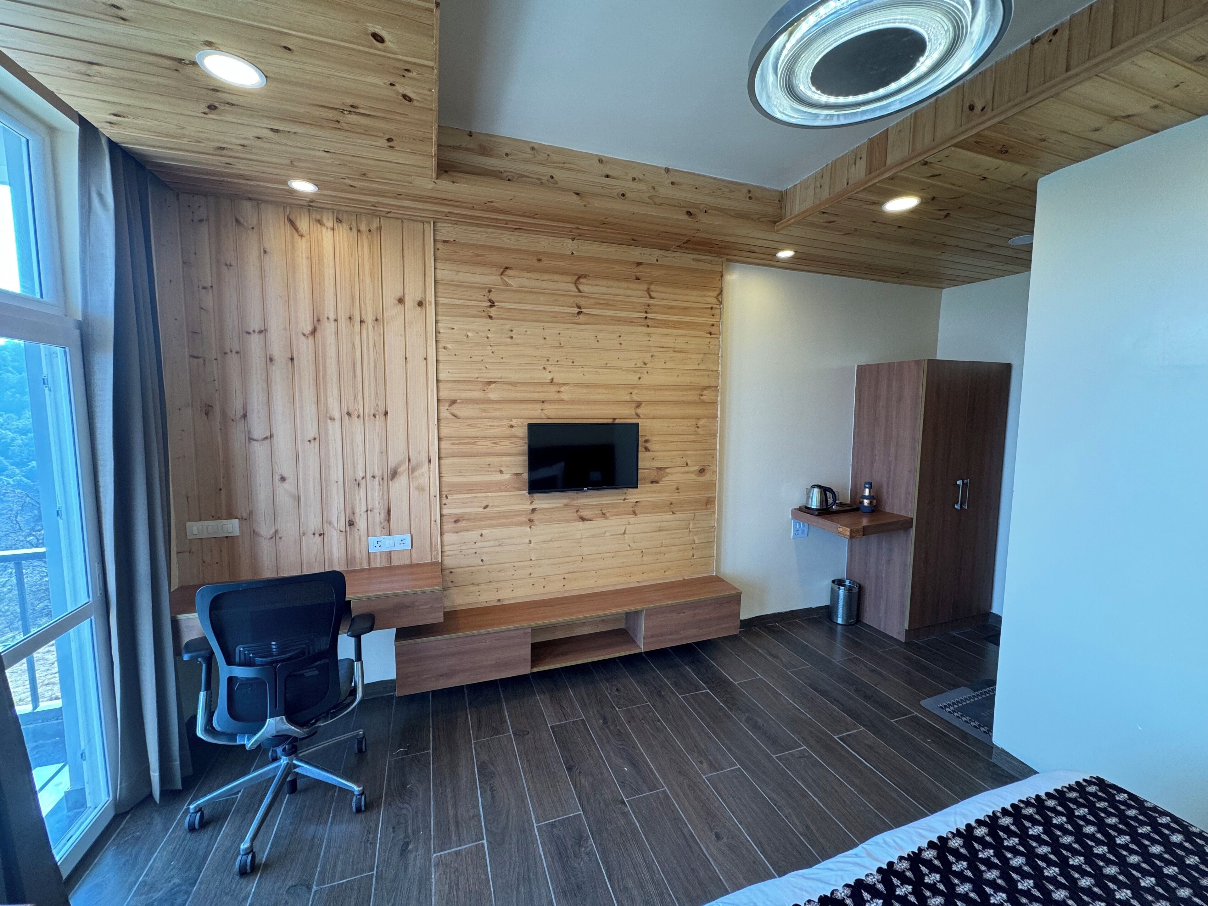 Une chambre moderne avec des murs lambrés, un téléviseur fixé au mur, un bureau, une chaise et une armoire.