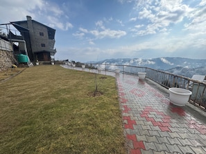 En bygning med en stenfassade, en belagt terrasse med røde og grå fliser samt udsigt til fjerne bjerge.