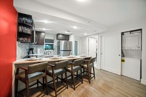 Een moderne keuken met een eethoek, barstoelen en een compacte was-droogcombinatie.