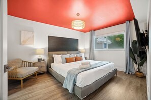 Un dormitorio moderno con una cama grande, una mesita de noche, una silla, una lámpara en el techo y una ventana con cortinas.