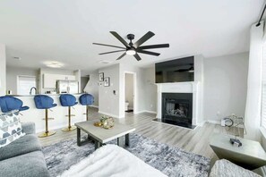 Ein modernes Wohnzimmer mit Kamin, einem Essbereich mit Barhocker und einer dahinterliegenden Küche.