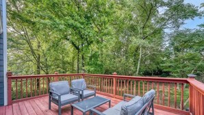 Een terras met buitenmeubilair, een rode balustrade en uitzicht op bomen.