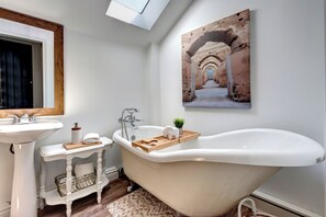 Un bagno con una vasca freestanding, un lavandino su piedistallo e un vassoio di legno sulla vasca.
