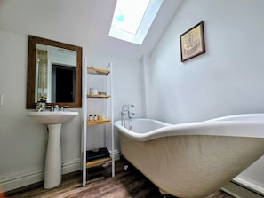 A bathroom with a freestanding bathtub, a pedestal sink, a mirror with a wooden frame, and a skylight.