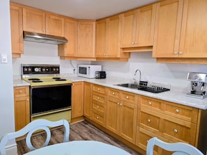 A kitchen with wooden cabinets, a stove, a microwave, a sink, and a coffee maker.