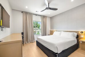 Una habitación de hotel con cama, escritorio, ventilador de techo y ventana con cortinas.