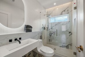Een moderne badkamer met een wit wastafelmeubel, toilet en een douchecabine met glazen wanden.