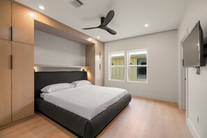 Een moderne slaapkamer met een bed, inbouwkast, plafondventilator en een aan de muur bevestigde televisie.