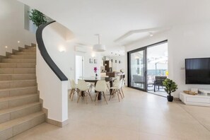 Ein modernes Interieur mit einer geschwungenen Treppe, einem Essbereich mit Stühlen, einem Flachbildfernseher und einem großen Fenster.