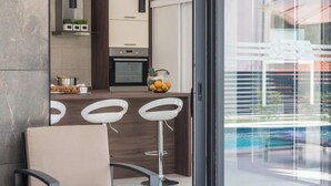 A modern kitchen with a bar area, a dining space with a chair, and a view of a pool through large windows. - Villa Blue Diamond (Biograd)