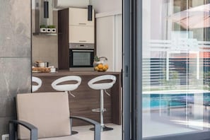 Eine moderne Küche mit Bar, einem Essbereich mit einem Stuhl und Blick auf einen Pool durch große Fenster.