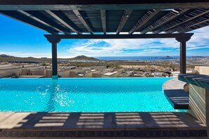 An infinity pool with a view of a cityscape and mountains. - Stylish Condo With Pool, Ocean Views, Fitness & Private Patio Grill (Cabo San Lucas)