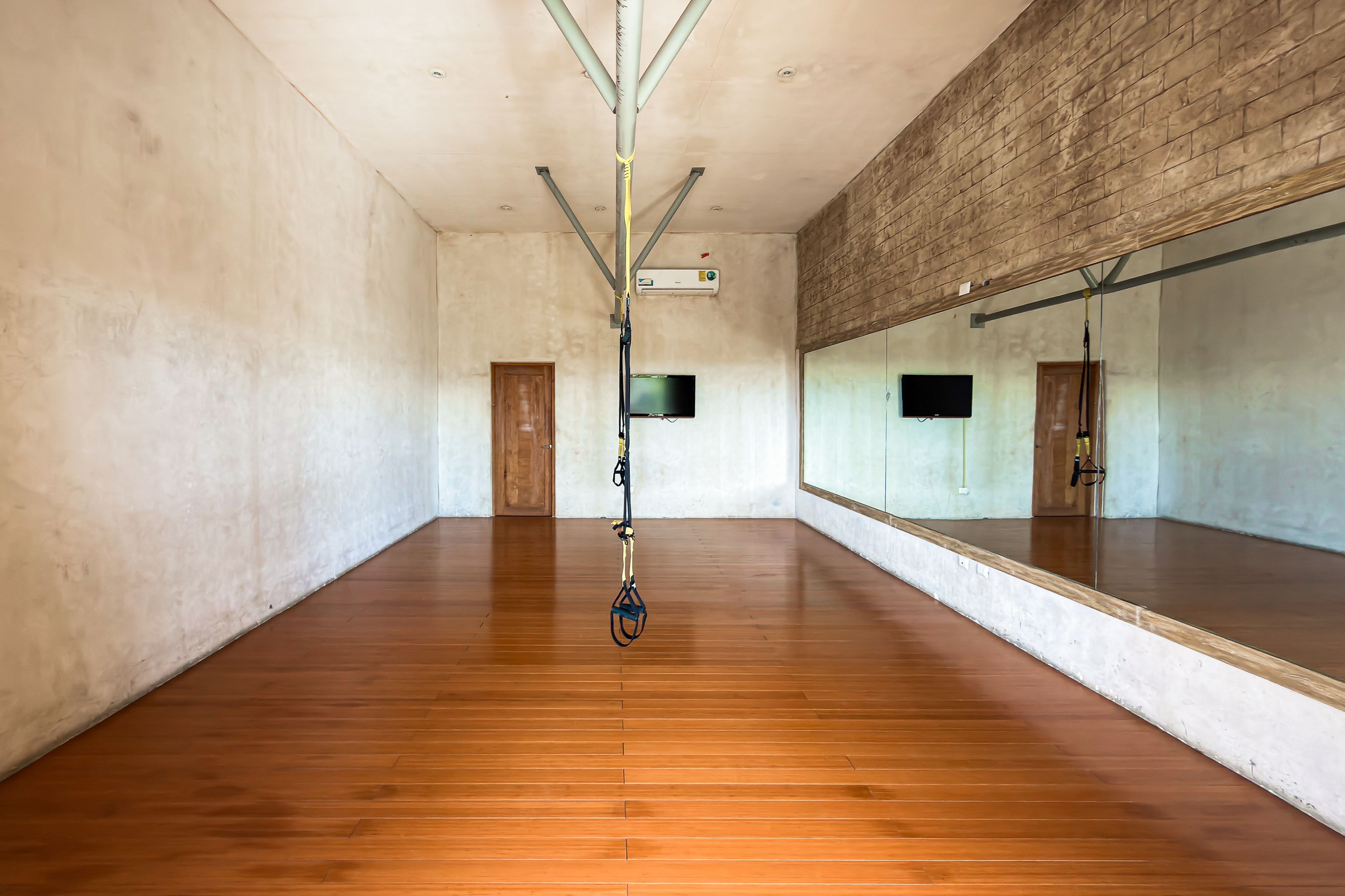 A spacious room with wooden flooring, a large mirror, and a ceiling-mounted pulley system.