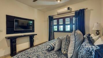 A bedroom with a bed, a TV mounted on the wall, a window with curtains, and a ceiling fan.