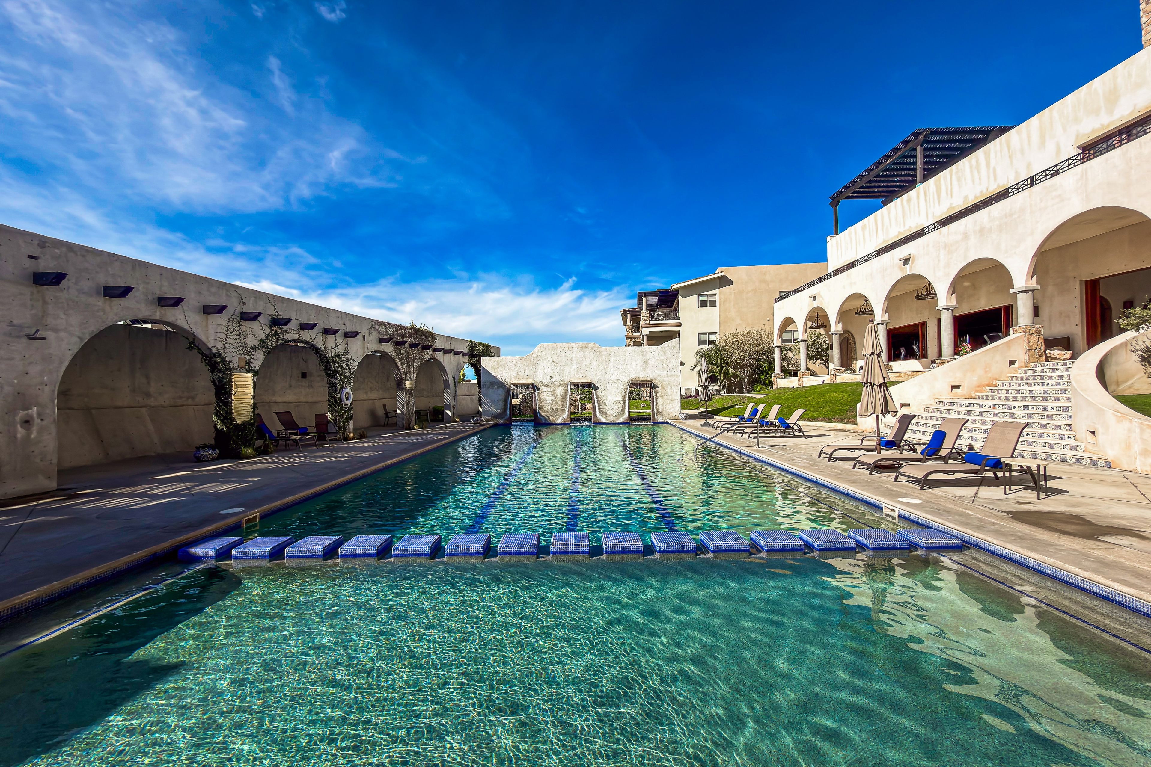 A pool area with clear water, lounge chairs, and arched walkways.