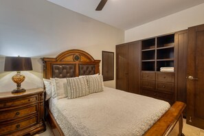 A bedroom with a large bed, wooden headboard, a nightstand with a lamp, and built-in wardrobes. - Stylish Condo With Pool, Ocean Views, Fitness & Private Patio Grill (Cabo San Lucas)