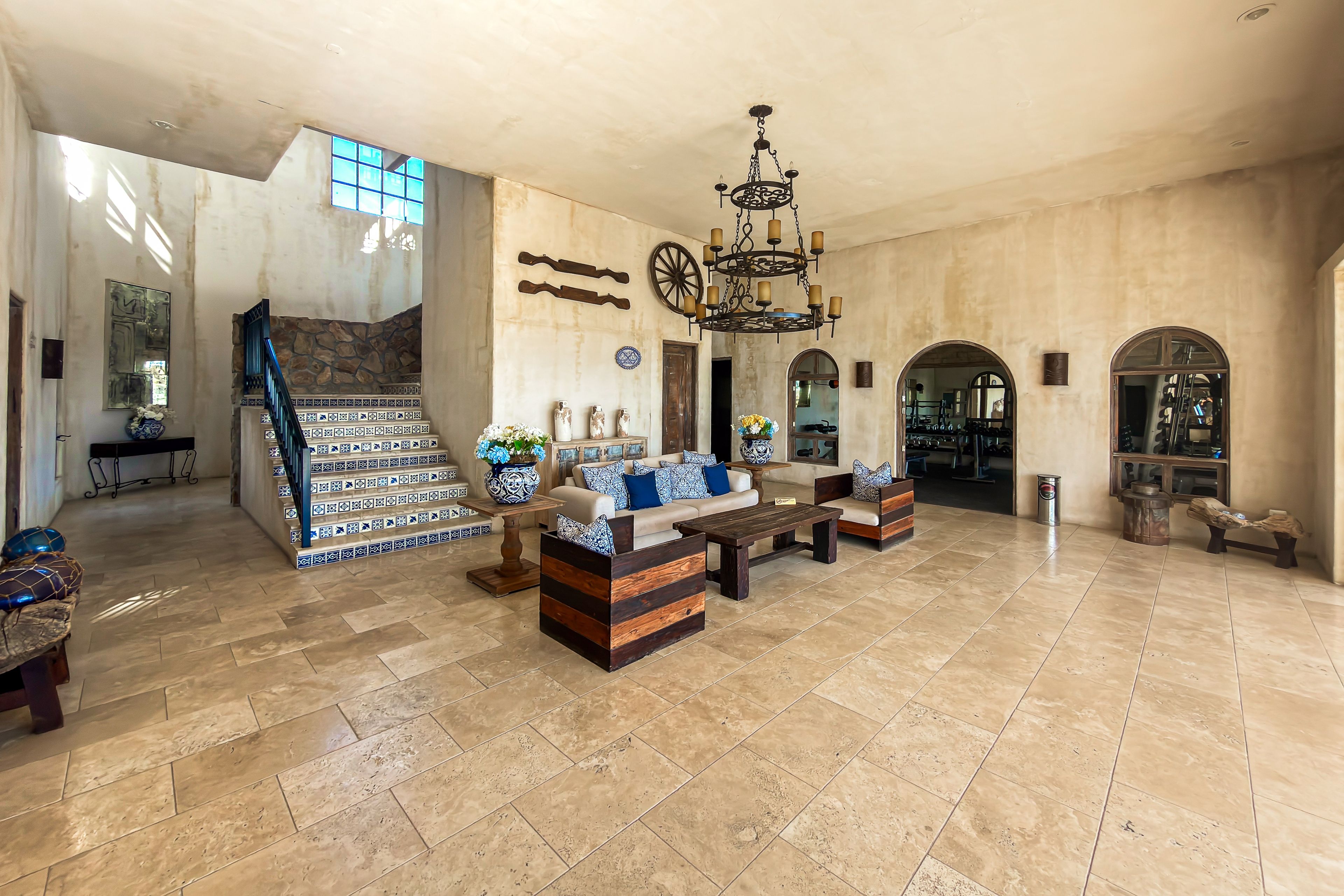 A spacious living area with a stone fireplace, a staircase, and a chandelier.