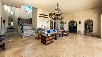 A spacious living area with a stone fireplace, a staircase, and a chandelier.