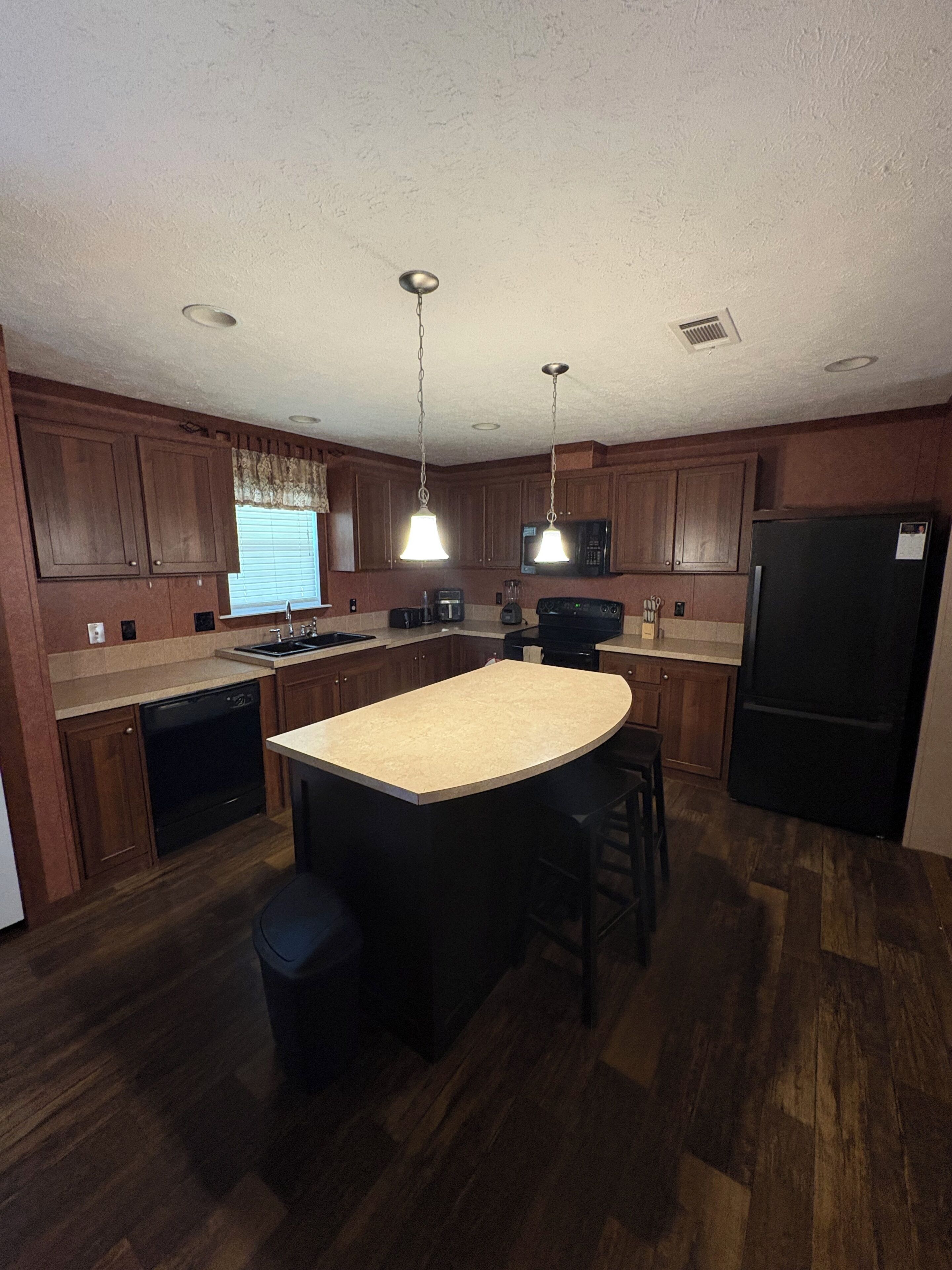 A kitchen with wooden cabinets, a central island, a refrigerator, and a microwave.. 3-bedroom farmhouse in wonderful Mannford with AC comfort Near Keystone Lake