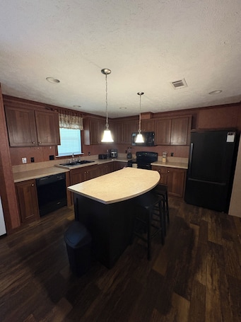 A kitchen with wooden cabinets, a central island, a refrigerator, and a microwave.. 3-bedroom farmhouse in wonderful Mannford with AC comfort Near Keystone Lake