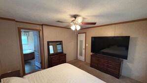 Una camera da letto con un letto, una cassettiera, un televisore, una ventola a soffitto e una porta che dà su un'altra stanza.