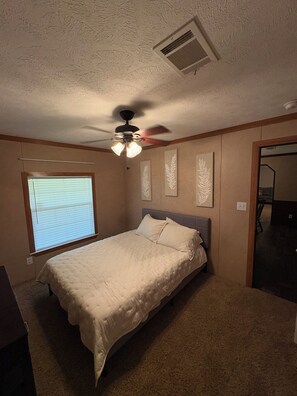 A bedroom with a bed, ceiling fan, window with blinds, and wall-mounted artwork. - 3-bedroom farmhouse in wonderful Mannford with AC comfort Near Keystone Lake (Mannford)