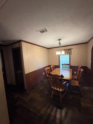 Un comedor con una mesa y sillas de madera, un candelabro y una ventana con persianas.