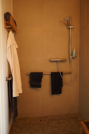 En dusch med ett justerbart duschhuvud, en handdukshängare med handdukar och en tvåldispenser på väggen.