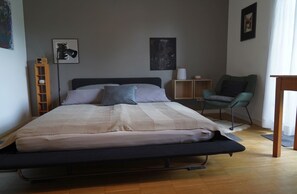 A bedroom with a bed, a chair, a bedside table, and artwork on the walls. - Vacation apartment with flair and terrace with a view of the flower and herb garden (Hetzerath)