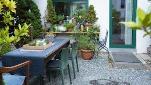 Un patio al aire libre con una mesa lista para comer, rodeado de macetas con plantas y varios objetos decorativos.